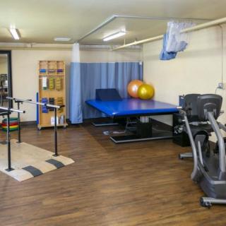 A rehabilitation therapy room equipped with parallel bars, a therapy table, medicine balls, and an exercise bike.