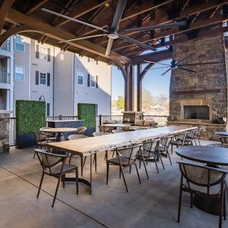 An inviting outdoor patio area with tables and chairs, a fireplace, and string lights under a covered structure.