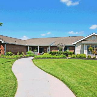 A suburban house with a well-manicured lawn and a winding pathway under a clear blue sky.