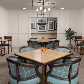 A cozy dining room with neatly arranged tables and chairs, featuring a decorative chandelier and wall art.
