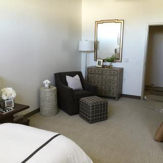 A cozy bedroom corner with a chair, ottoman, and a dresser topped with a mirror and lamp.