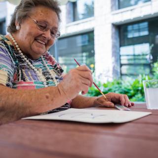 An elderly woman enjoying a painting session outdoors, smiling as she creates art.