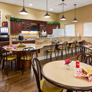 A cozy cafe dining area with round tables, chairs, pendant lights, and a beverage station.