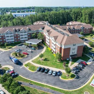 Aerial view of a large residential building surrounded by greenery and parking spaces.
