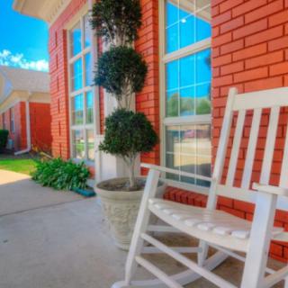 A peaceful porch with a white rocking chair and potted plants in front of a red brick wall.