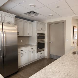 A modern kitchen interior featuring white cabinets, a stainless steel refrigerator, and built-in ovens.