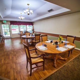 A cozy dining area with wooden floors and well-arranged tables and chairs, illuminated by a chandelier.