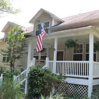 A charming house with a front porch, featuring an American flag and surrounded by greenery.