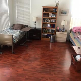 A tidy bedroom with two beds, hardwood flooring, and a bookshelf.