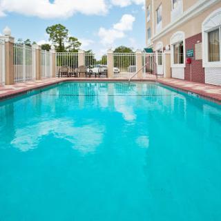 A serene outdoor swimming pool surrounded by greenery and a clear blue sky.