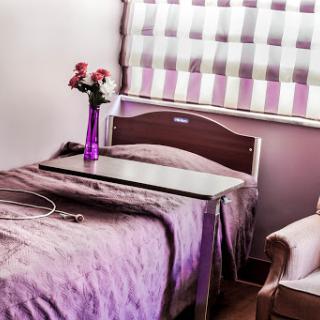 A cozy hospital room featuring a neatly made bed, a bedside table, and fresh flowers in a purple vase.