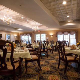 An elegant dining room with neatly arranged tables and chairs, illuminated by chandeliers.