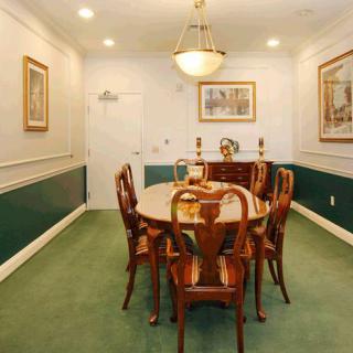 A traditional dining room with a wooden table and chairs, illuminated by a chandelier and adorned with wall art.
