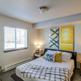 A cozy bedroom with a neatly made bed, modern artwork, and ample natural light.