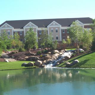 A scenic view of a building with a pond and waterfall in the foreground, surrounded by lush greenery.