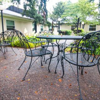A cozy outdoor seating area featuring a metal table and chairs surrounded by lush greenery.