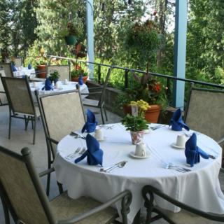 A beautifully set table on an outdoor restaurant patio surrounded by lush greenery and flowers.