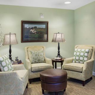 A cozy living room with comfortable chairs and lamps, featuring a painting on the wall.