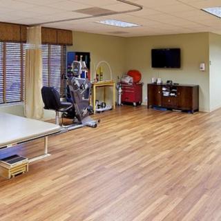 A spacious physical therapy room equipped with various rehabilitation tools and a wooden floor.