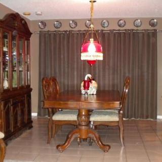 A dining room with a wooden table and chairs, surrounded by curtains and illuminated by a chandelier.