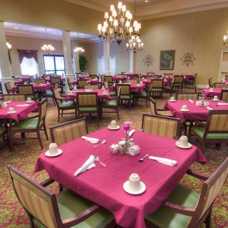 A spacious dining room with elegantly set tables and chandeliers.