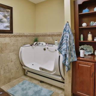 A bathroom with an accessible bathtub, surrounded by tiled walls and a wooden shelf stocked with toiletries.