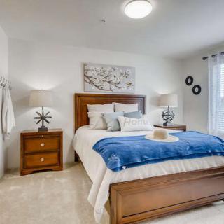 A modern and cozy bedroom featuring a neatly made bed with a blue blanket, flanked by wooden nightstands and stylish lamps. The room is decorated with wall art above the headboard.