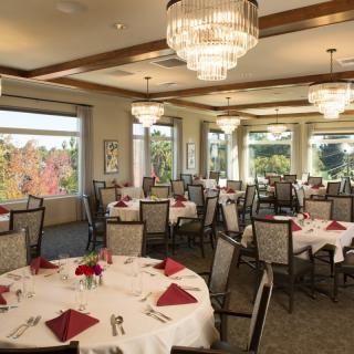 An elegant banquet hall with round tables set for dining, featuring chandeliers and large windows overlooking a scenic view.