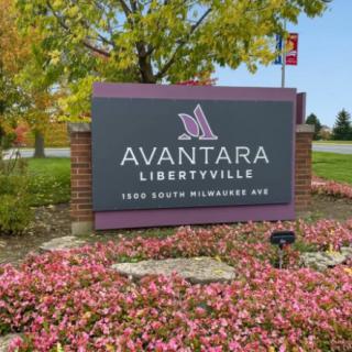 Entrance sign for Avantara Libertyville surrounded by colorful flowers and trees.