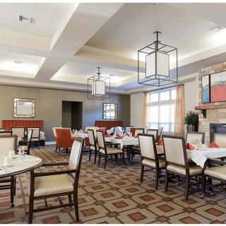 A well-lit dining room with neatly arranged tables and chairs, featuring a patterned carpet and modern lighting fixtures.