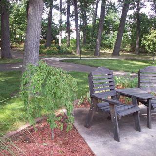 A peaceful garden setting with wooden chairs and a table surrounded by trees.