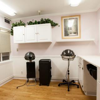 A neatly arranged salon interior featuring hair drying stations, white cabinets, and wooden flooring.