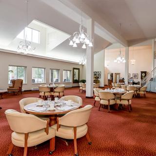 A spacious and elegantly designed dining area with multiple round tables and comfortable seating, illuminated by chandeliers.