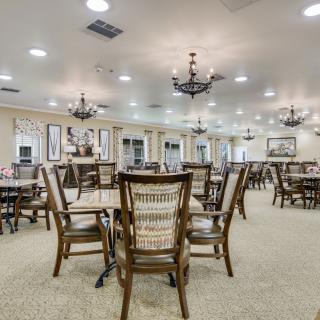A spacious dining hall with neatly arranged tables and chairs under elegant chandeliers.