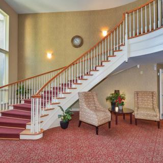 A classic interior featuring a curved staircase with red carpeting, accompanied by a cozy seating area and decorative plants.