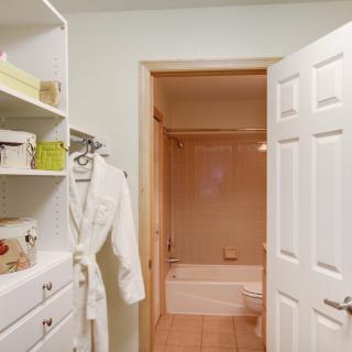 A view of a bathroom through an open closet, showing a robe hanging and neatly organized shelves.