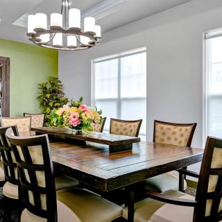 A modern dining room with a large wooden table, upholstered chairs, and a stylish chandelier.