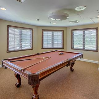 A well-lit game room featuring a classic pool table with cue sticks placed on top.
