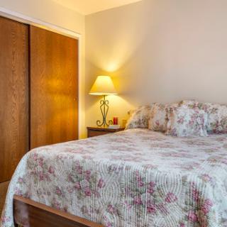 A cozy bedroom featuring a floral-patterned bedspread, a bedside lamp, and wooden closet doors.
