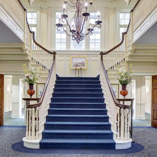 A grand staircase with a blue carpet and elegant chandelier in a luxurious interior setting.