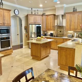 Spacious kitchen with wooden cabinets and a central island, featuring stainless steel appliances and a tile floor.