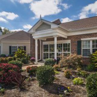 A charming single-story house with a well-maintained garden under a bright blue sky.