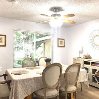 A cozy dining room featuring a well-set table, comfortable chairs, and ample natural light from the windows.