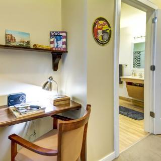 A small workspace with a desk, chair, and lamp next to an open door leading to a bathroom.