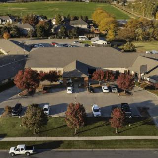 An aerial view of a building with a parking lot, surrounded by trees in autumn colors.