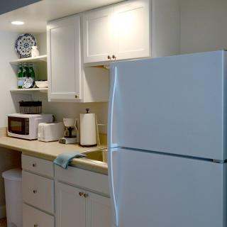 A tidy kitchen with white cabinets, featuring a refrigerator, microwave, and various kitchen appliances on the countertop.