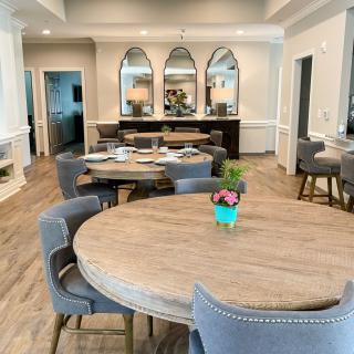 A modern dining area with round tables and upholstered chairs, featuring mirrors on the walls and wood flooring.