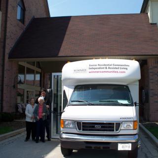A group of people stands near a white van parked in front of a building.