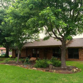 A charming residential house surrounded by lush greenery and well-maintained landscaping.