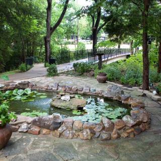 A peaceful garden pond surrounded by a stone path and lush greenery.